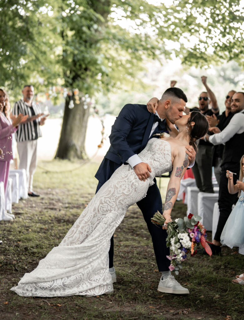 Hochzeitspaar küsst sich umrundet von jubelnden Gästen